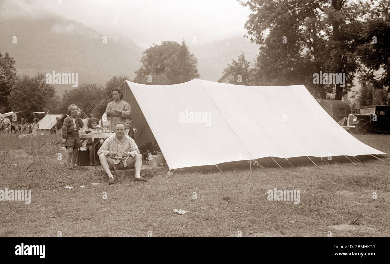 Vacances et conges payes : une famille francaise prenant son petit-dejeuner (tartines) devant la tente dans un camping, en arriere plan voiture et rou Stock Photo
