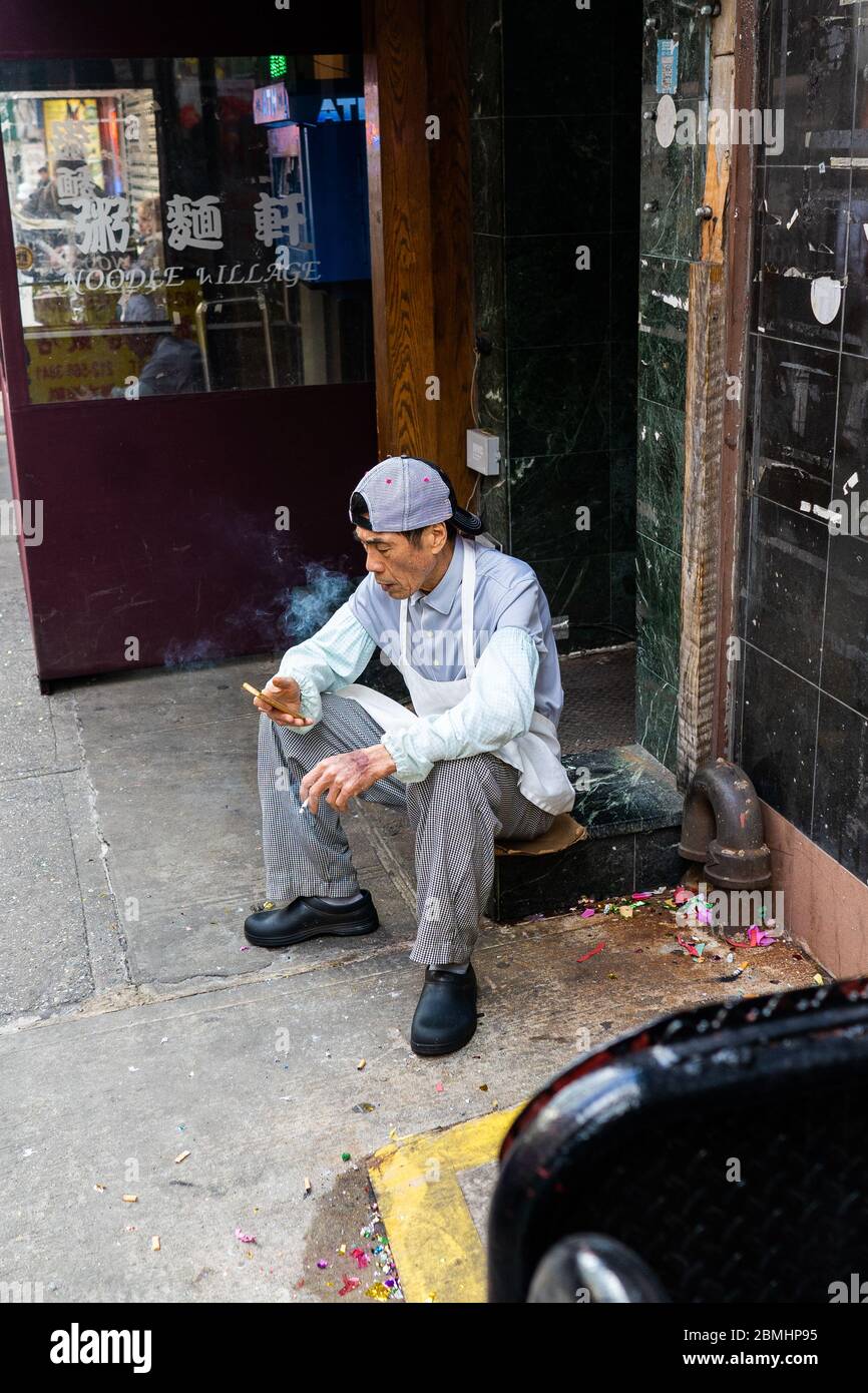 Chinatown, New York, USA - February 8 2020: Asian Chinese Man Sitting and  Smoking Cigarette in Chinatown During Lunar Year Parade Stock Photo