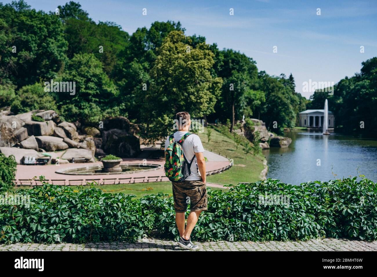 Sofia Park, Ukraine. Man with a backpack in a landscaped park in summer. Man turned his back on the background of the lake with a fountain. Stock Photo