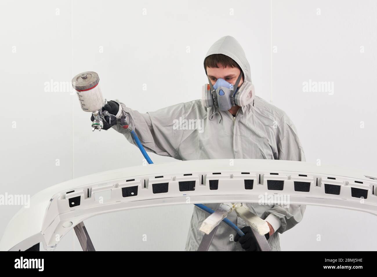 Mechanic painting bumper of a car with sprayer in painting booth in repair auto service Stock Photo