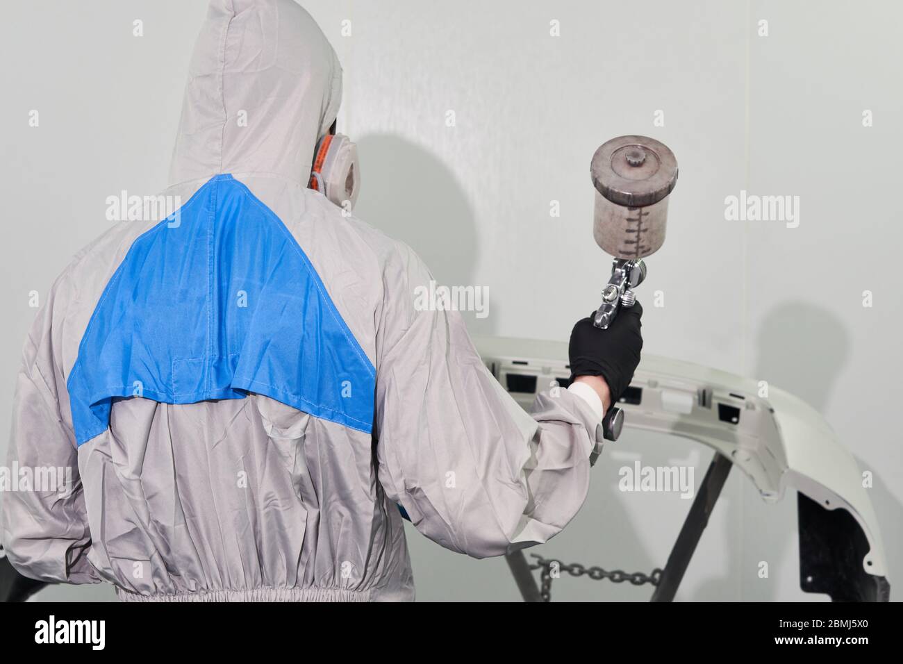 Mechanic painting bumper of a car with sprayer in painting booth in repair auto service Stock Photo