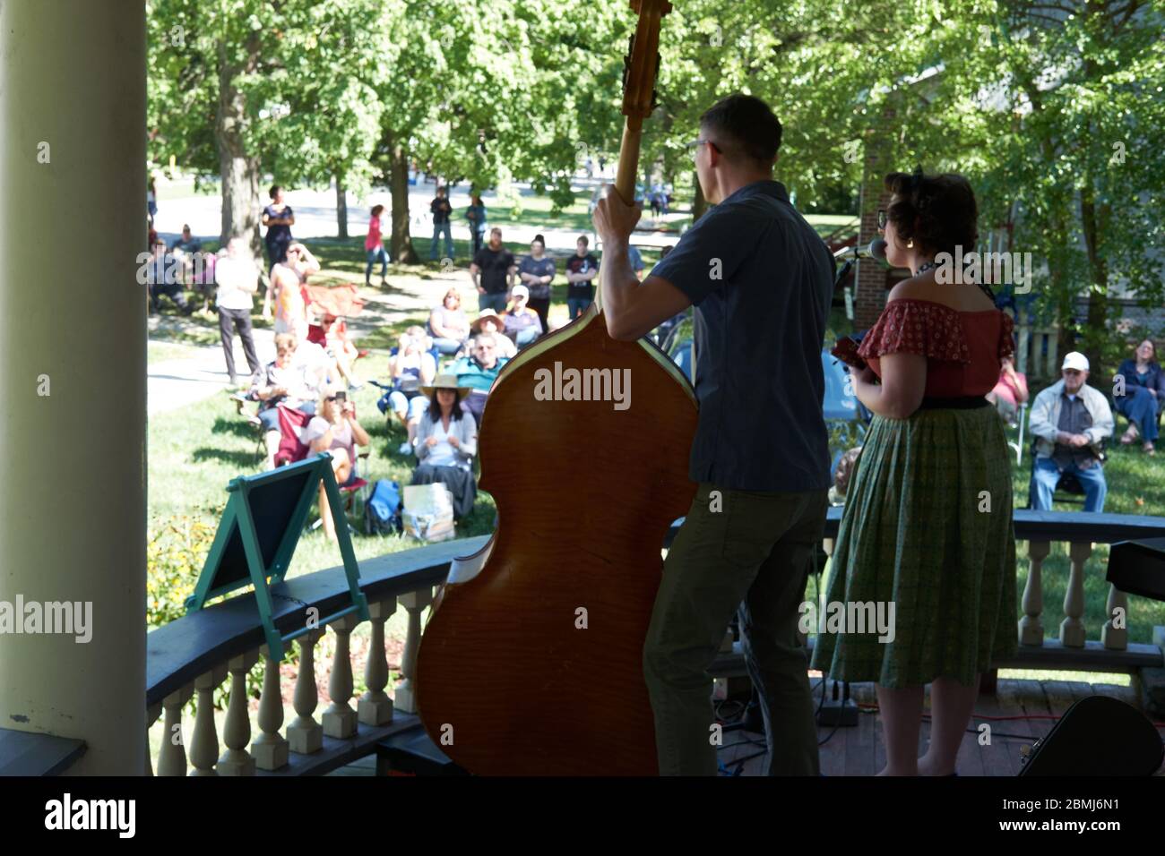 Attractive young retro couple singing and playing double bass and ukulele to a crowd outdoors at a Summer porch concert event in a historic residentia Stock Photo