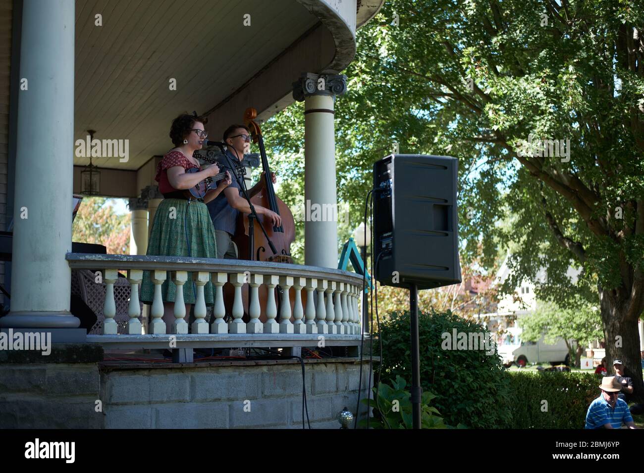 Attractive young retro couple singing and playing double bass and ukulele to a crowd outdoors at a Summer porch concert event in a historic residentia Stock Photo