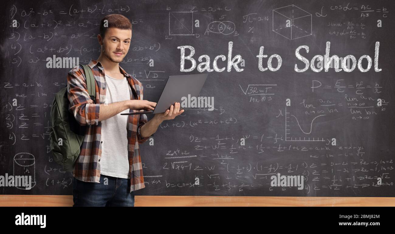 Male student holding a laptop computer in front of a blackboard with ...