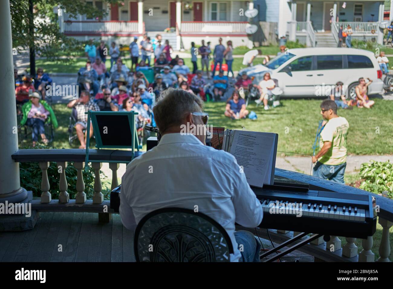 man wearing white shirt and playing an electric piano keyboard to a crowd outdoors at a Summer porch concert in a historic residential neighborhood Stock Photo