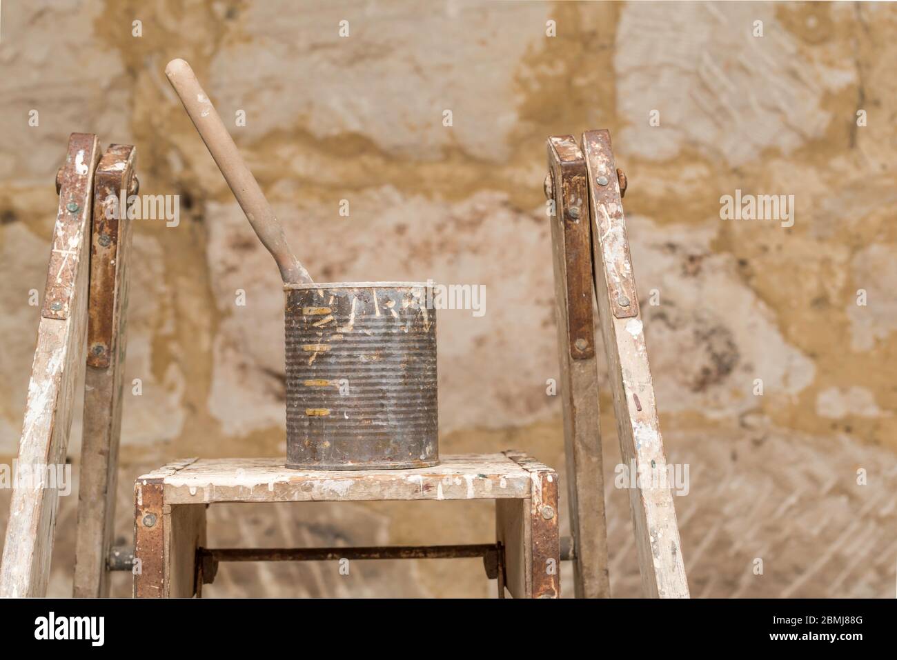A single paint brush sitting in an old canned fruit tin covered in paint and resting on an old painters ladder in morning sunlight Stock Photo