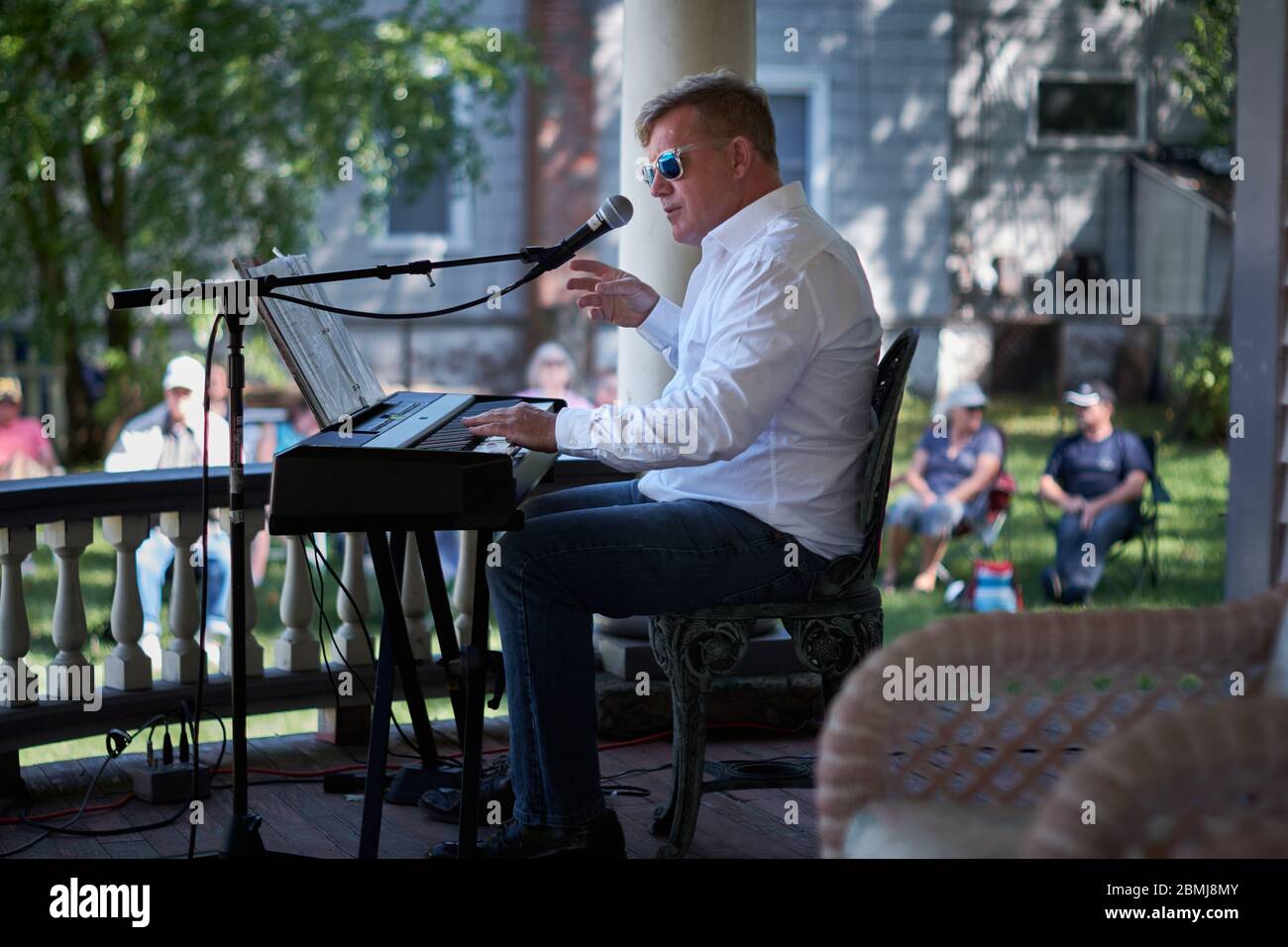 caucasian man wearing white shirt playing an electric keyboard to a crowd outdoors at a Summer porch concert in a historic residential neighborhood Stock Photo