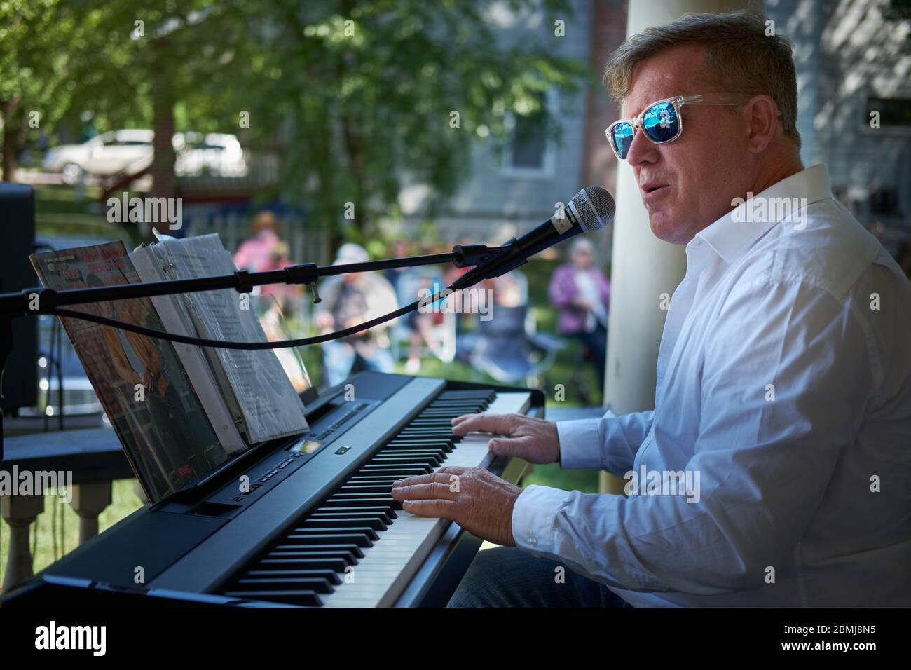 caucasian man wearing white shirt playing an electric keyboard to a crowd outdoors at a Summer porch concert in a historic residential neighborhood Stock Photo