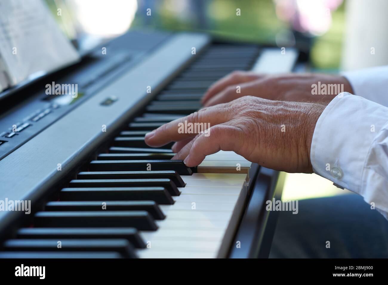 Close up photo of the hands of a white caucasian man wearing a white shirt playing an electric piano keyboard outdoors. Stock Photo