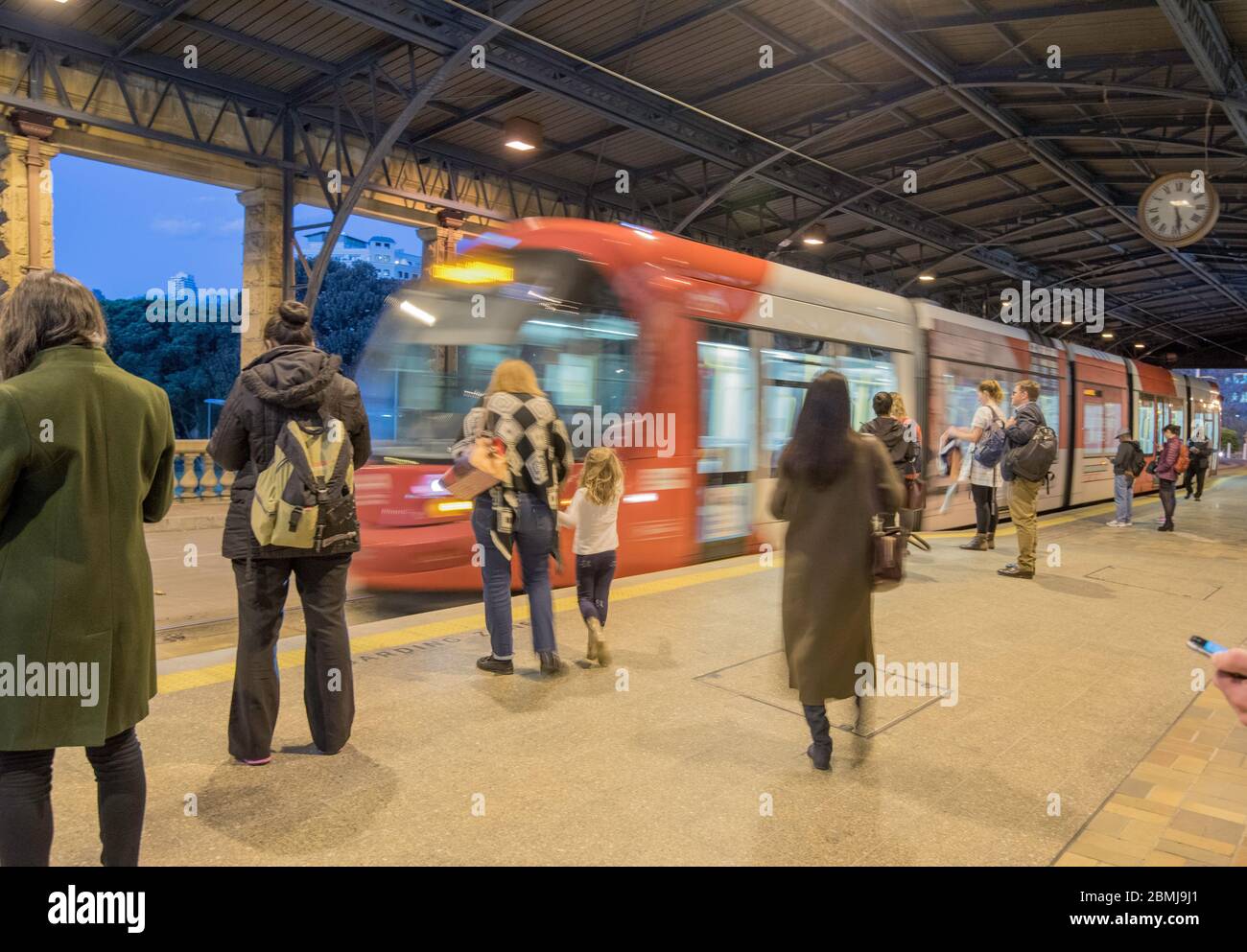 Commuters waiting to board an approaching light rail tram at Central Station during the evening commute in winter in Sydney, Australia Stock Photo