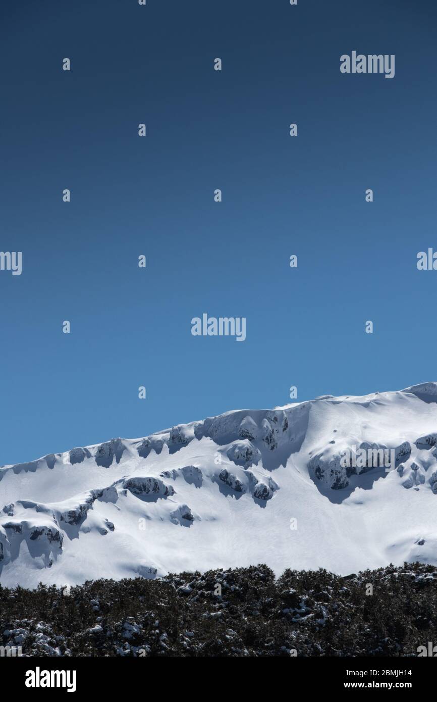 Close-up view of snow capped mountain ridge with a blue sky background ...