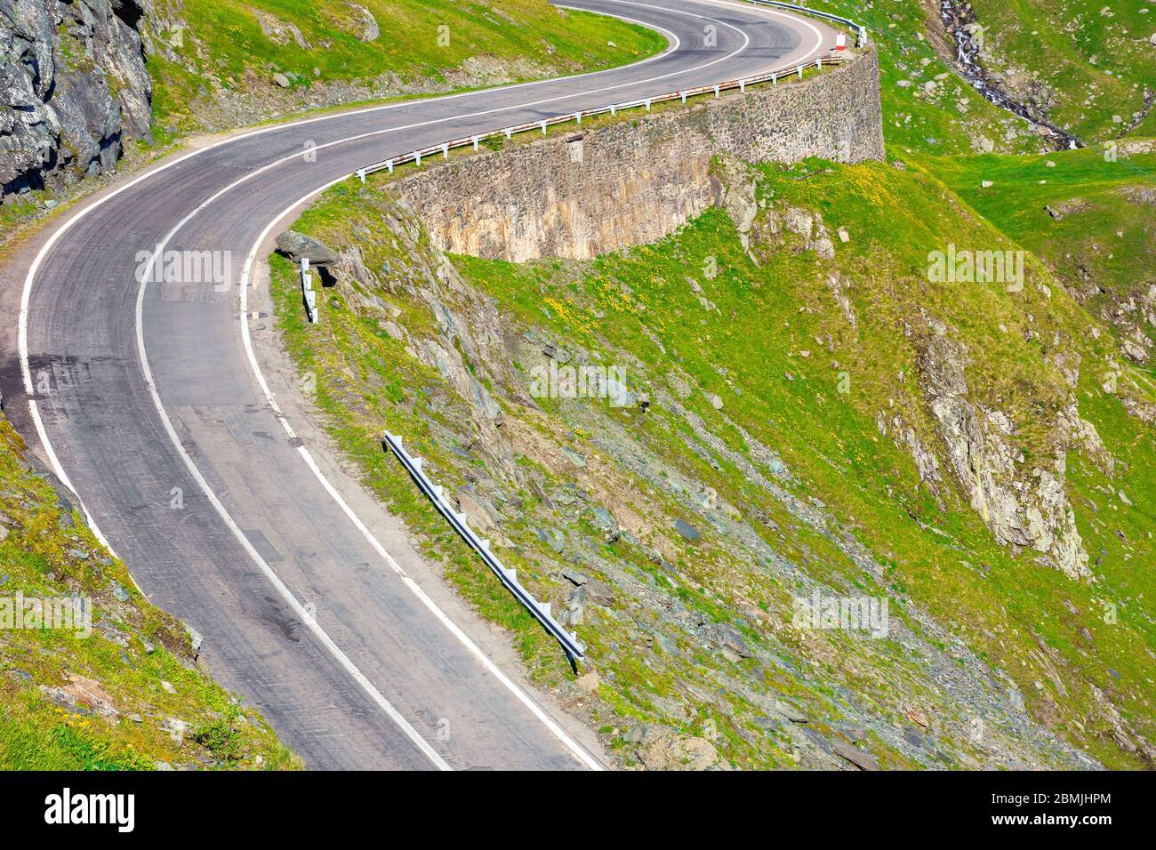 winding mountain road on a sunny day. empty highway run through valley. open vista in the distance. great european journey in summertime concept. Stock Photo