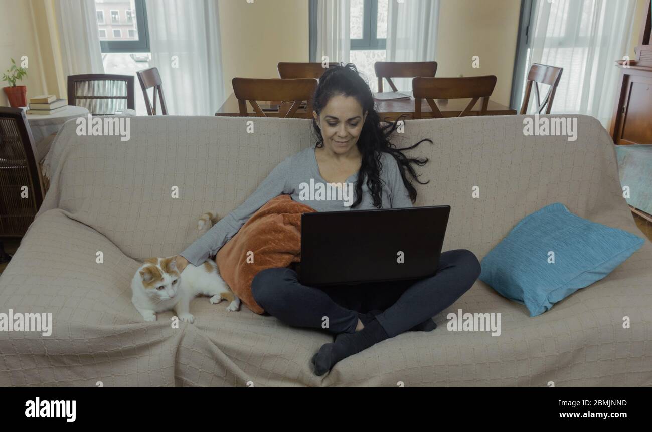 Brunette woman teleworking at home on a sofa with her cat next to her Stock Photo