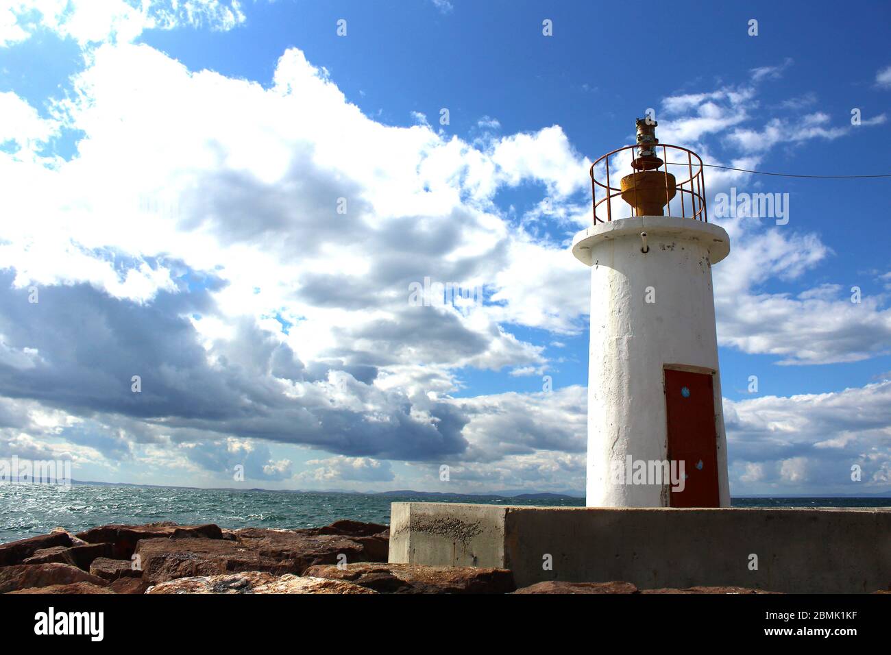 A port made of rocks and a white lighthouse. Wavy sea and cloudy windy weather. Stock Photo