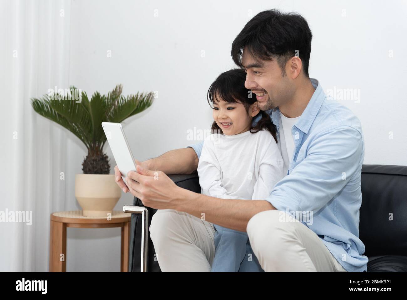 A pair of young Asian father and daughter are using tablet in the living room Stock Photo