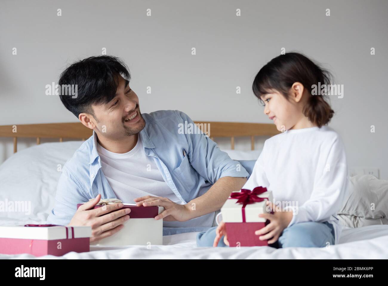 Young Asian dad is unpacking gifts on bed with daughter Stock Photo