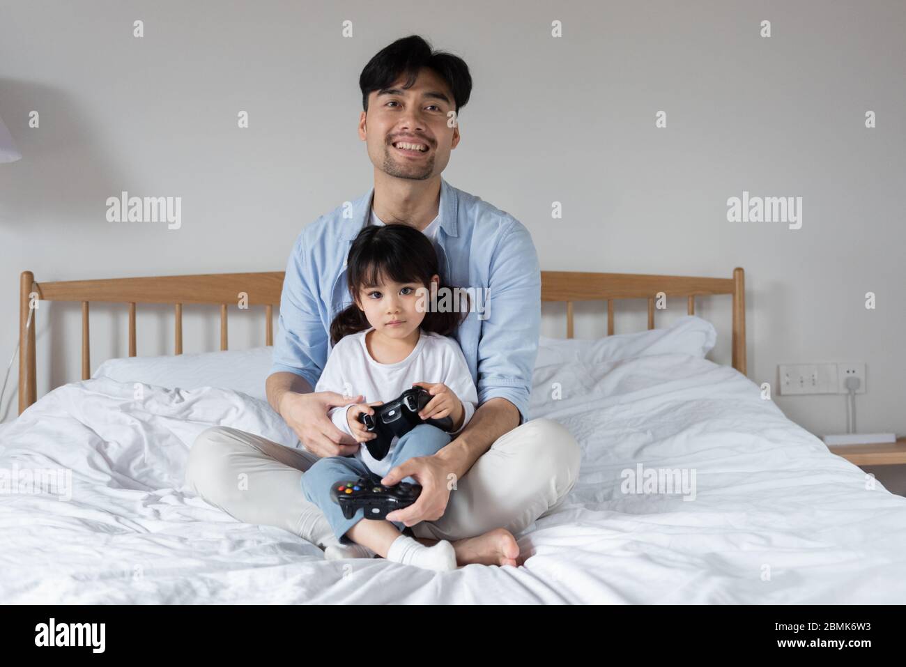 Young Asian dad is playing games on bed with daughter Stock Photo
