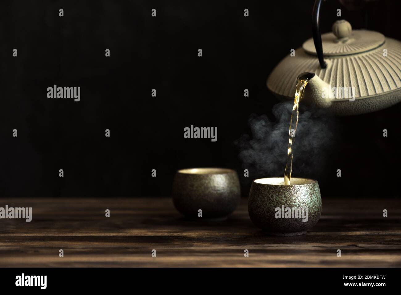 Teapot pouring tea into cups. Traditional japanese chinese iron teapot