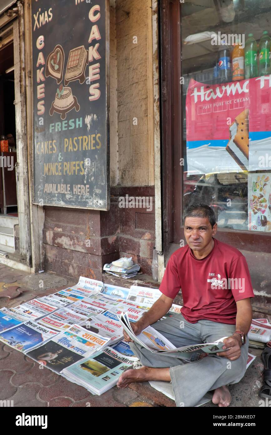 A neswspaper vendor having his papers spread out on the sidewalk outside a restaurant in Byculla, Mumbai, India Stock Photo