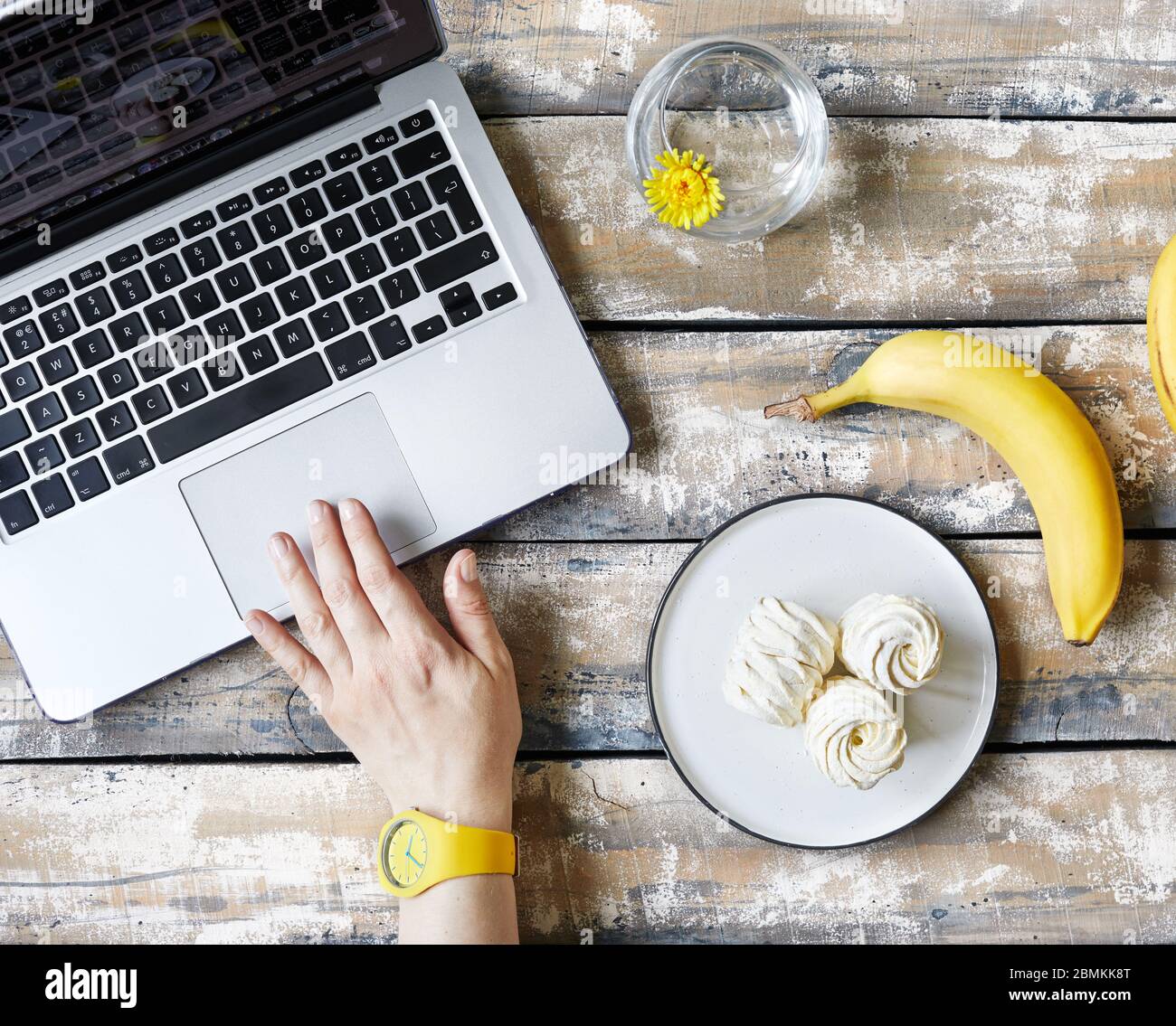Woman working from home and eating banana and sweet homemade Zephyr or Marshmallow from banana near laptop on wooden table top view.  Time for break Stock Photo