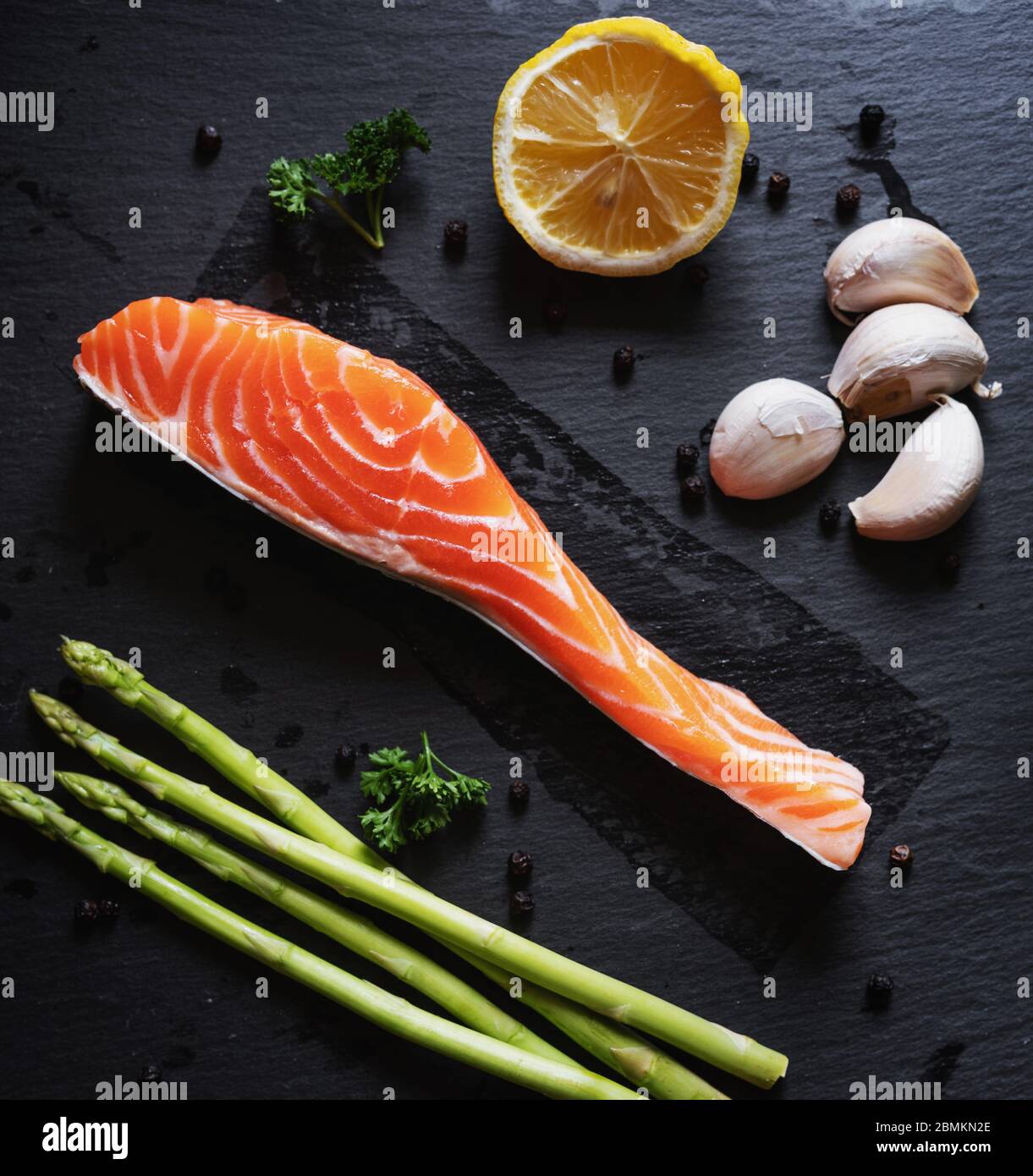 Fresh raw Salmon slice with herb and ingredients, on black slate texture background. Salmon fillet Stock Photo