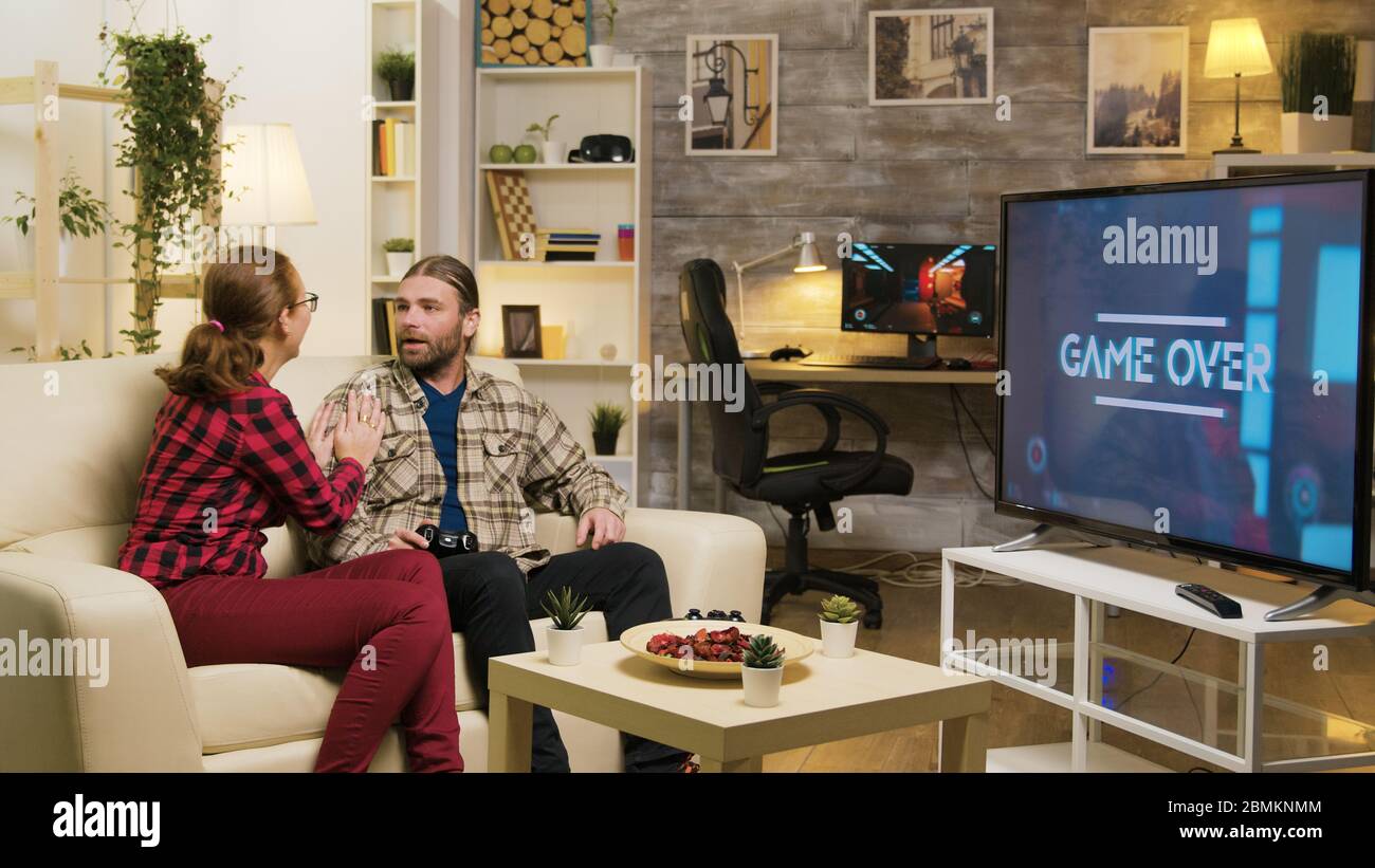 Game over for man while playing video games using wireless controller with his girlfriend next to him on the couch. Stock Photo