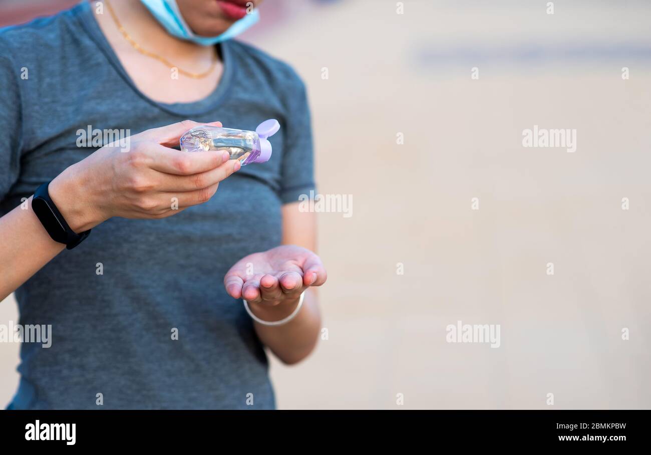 Woman using hand sanitizer on the street and wearing face mask as a covid 19 precaution outdoors Stock Photo