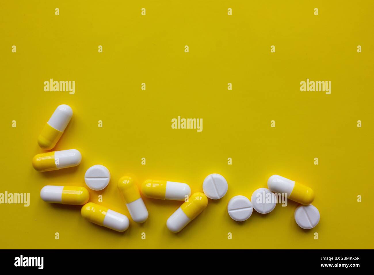 Yellow and white capsules and white pills on a yellow background Stock
