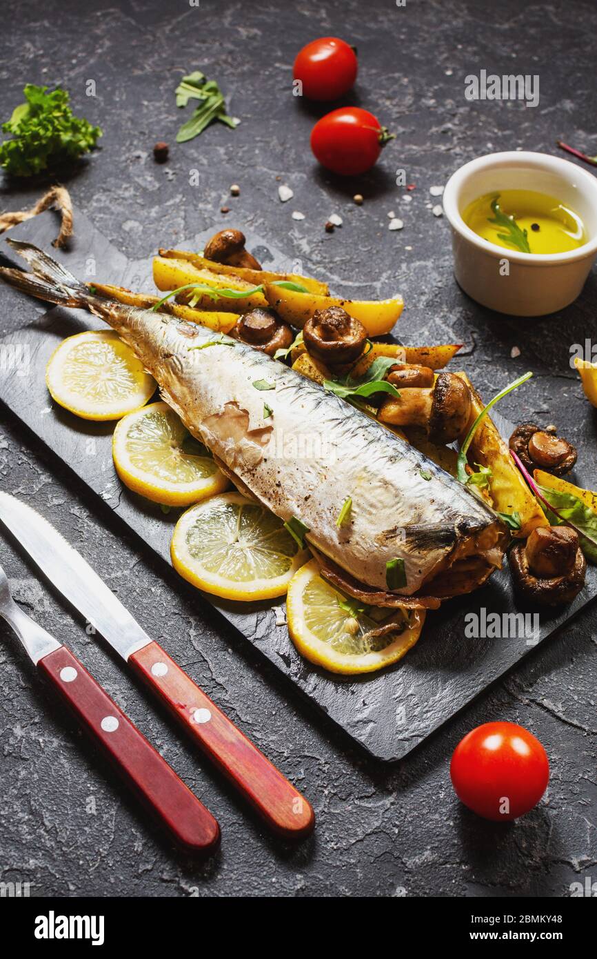 Baked mackerel with lemon, baked potatoes and mushrooms on black stone