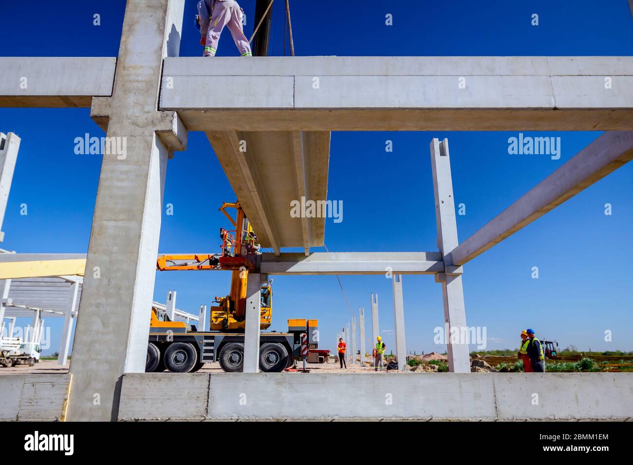Worker is helping mobile crane to manage concrete joist for assembly ...