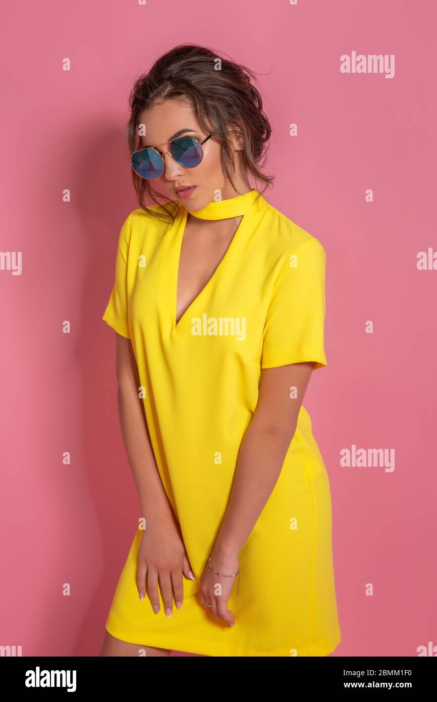 Beautiful girl wearing yellow dress and sunglasses posing on pink ...
