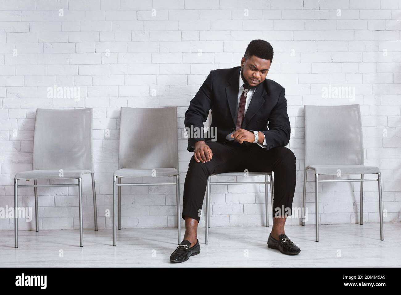 Millennial African American guy waiting for job interview, looking at his  watch in office lobby. Empty space Stock Photo - Alamy