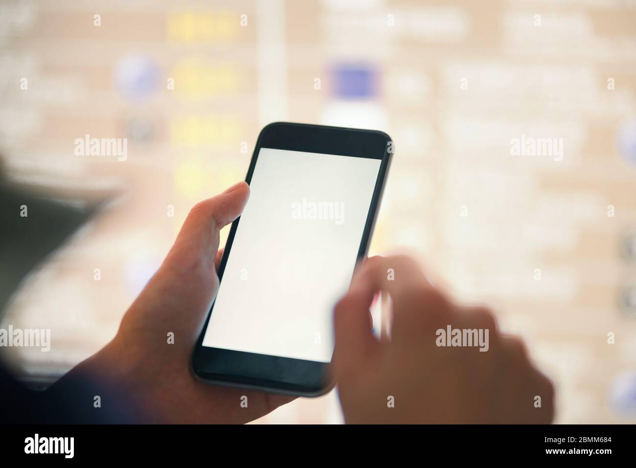 Mockup image of female hands holding black mobile phone with blank white screen over flight board in airport terminal Stock Photo