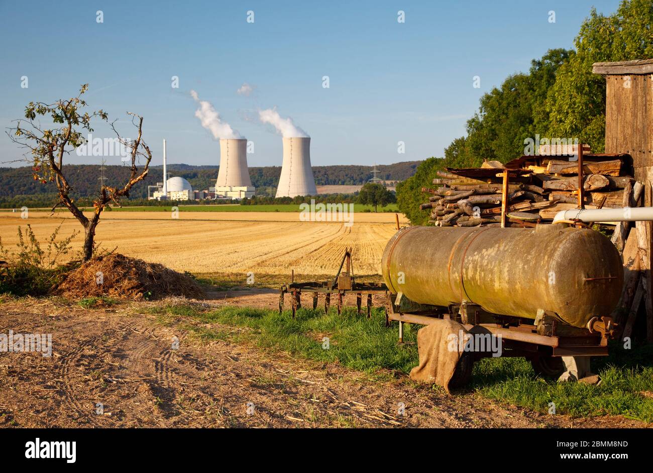 An apple tree and old agricultural machines in the foreground of a nuclear power plant, contrast between nature and environmental damage. Stock Photo