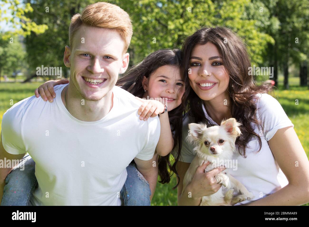 Happy smiling family of parents and daughter with pet dog in spring park Stock Photo