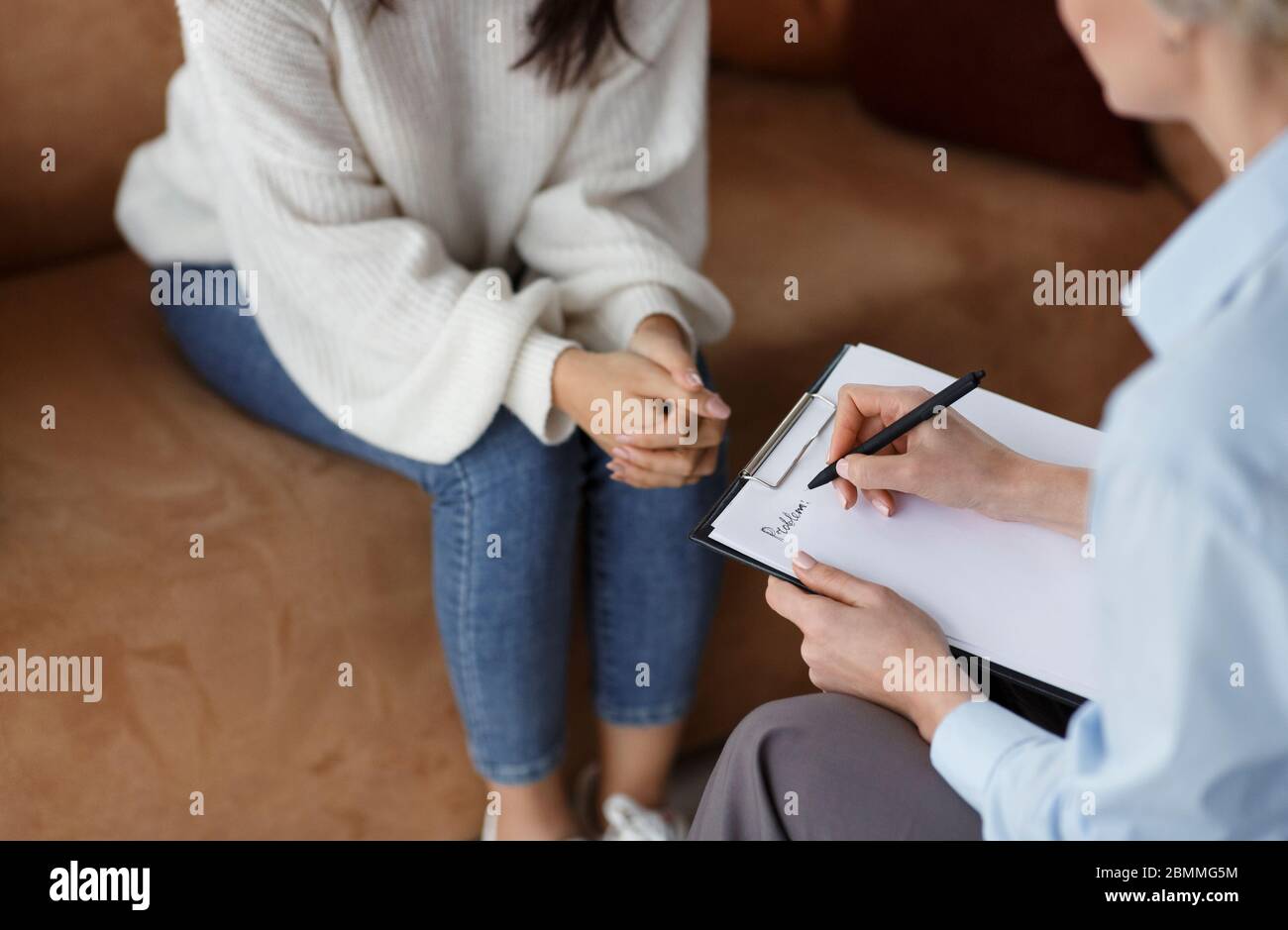 Unrecognizable Psychologist Talking With Client Taking Notes Sitting In Office Stock Photo