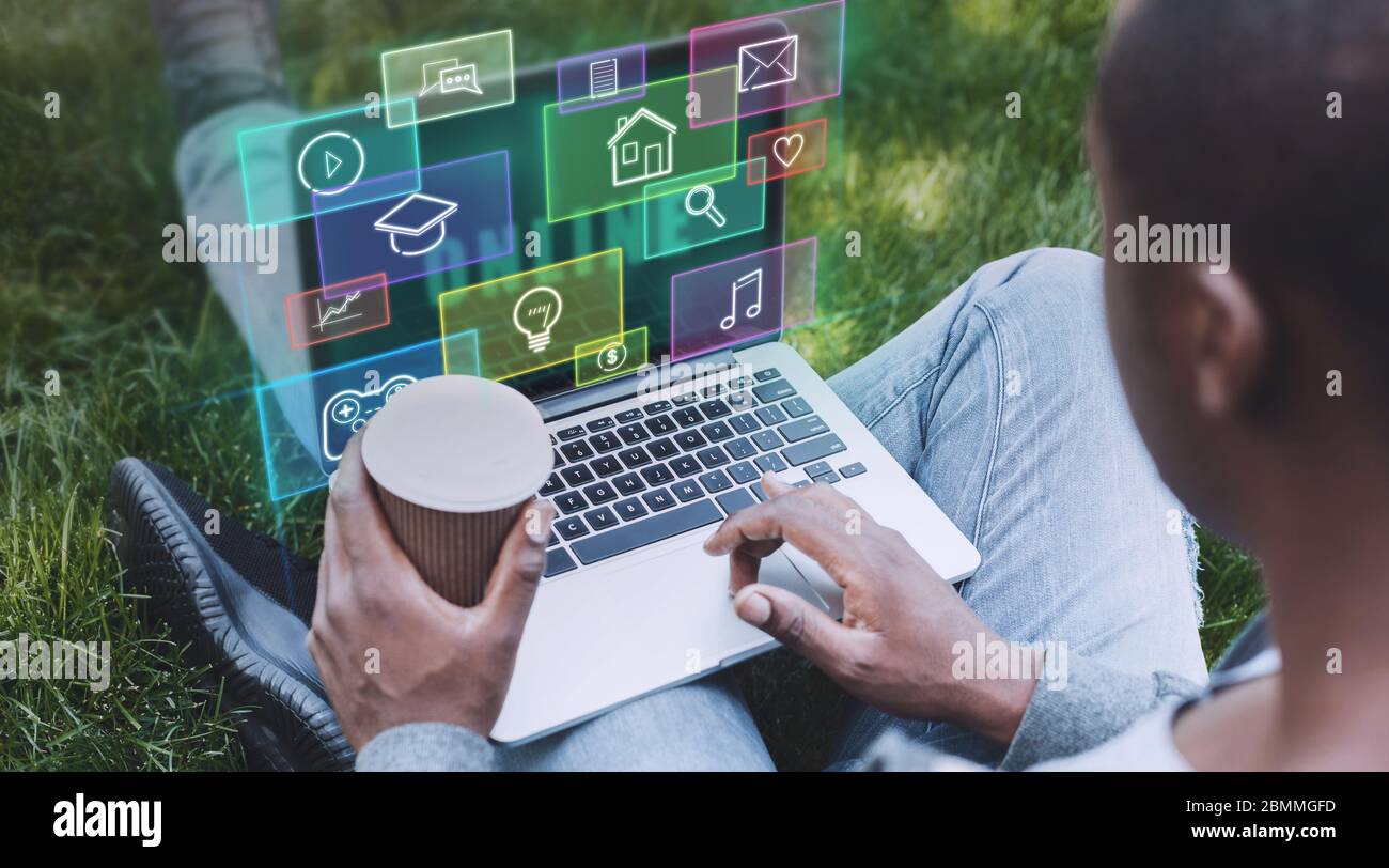 Black guy using internet on his laptop in park, collage with functional icons on virtual screen Stock Photo
