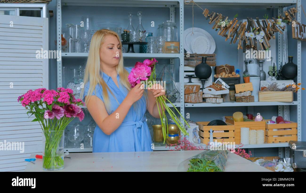 Professional floral artist, florist in blue dress sorting flowers - pink peonies for bouquet at workshop, flower shop. Floristry, handmade and small Stock Photo