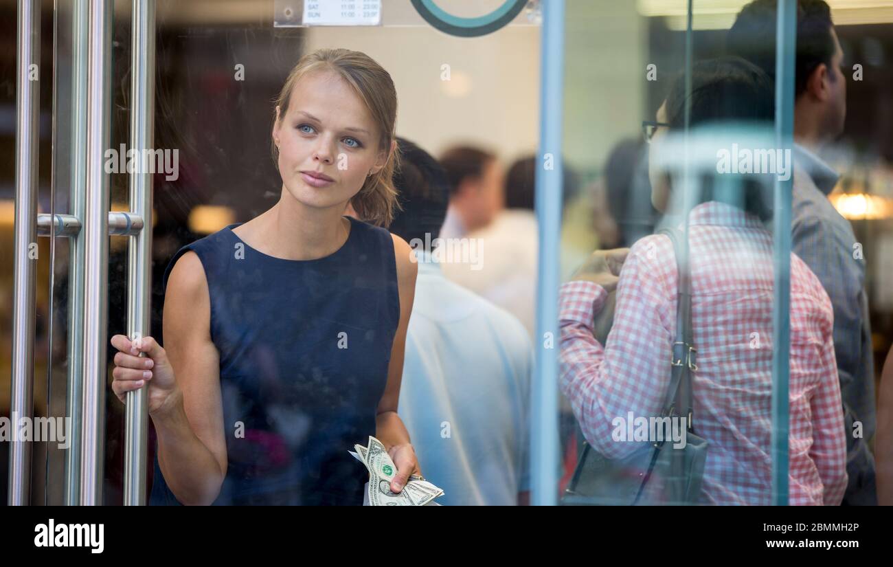 Pretty, young woman leaving a store/restaurant with cash in her hand after having paid for for the goods/food Stock Photo