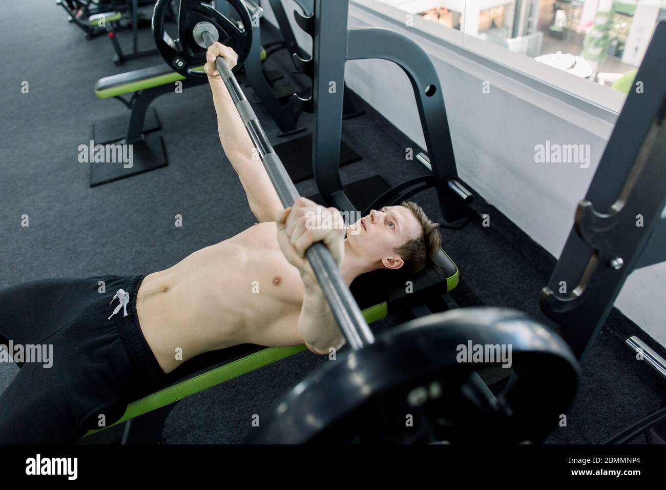 Young athletic man pumping up muscles on bench press in the gym. young