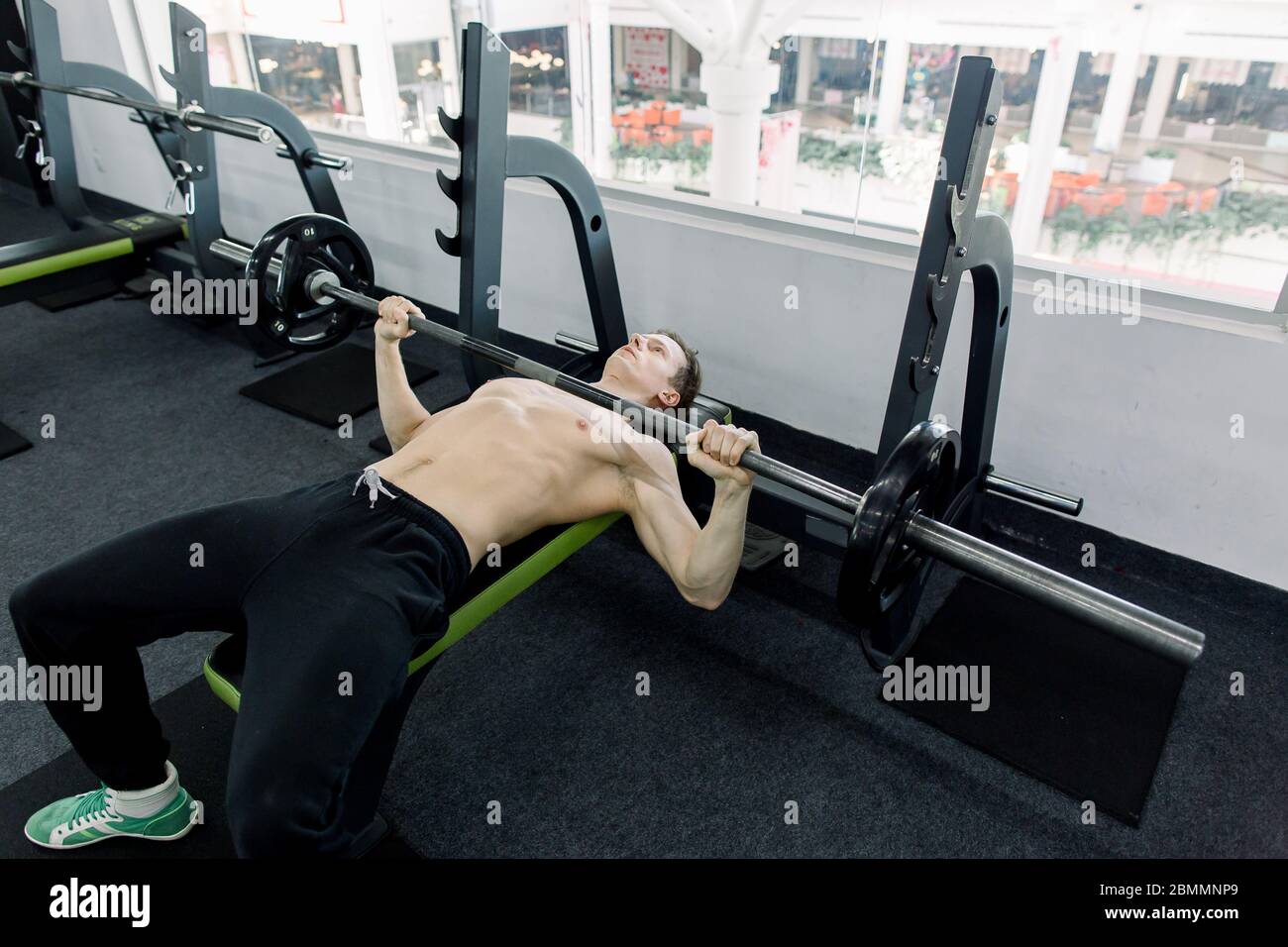 Young athletic man pumping up muscles on bench press in the gym. young