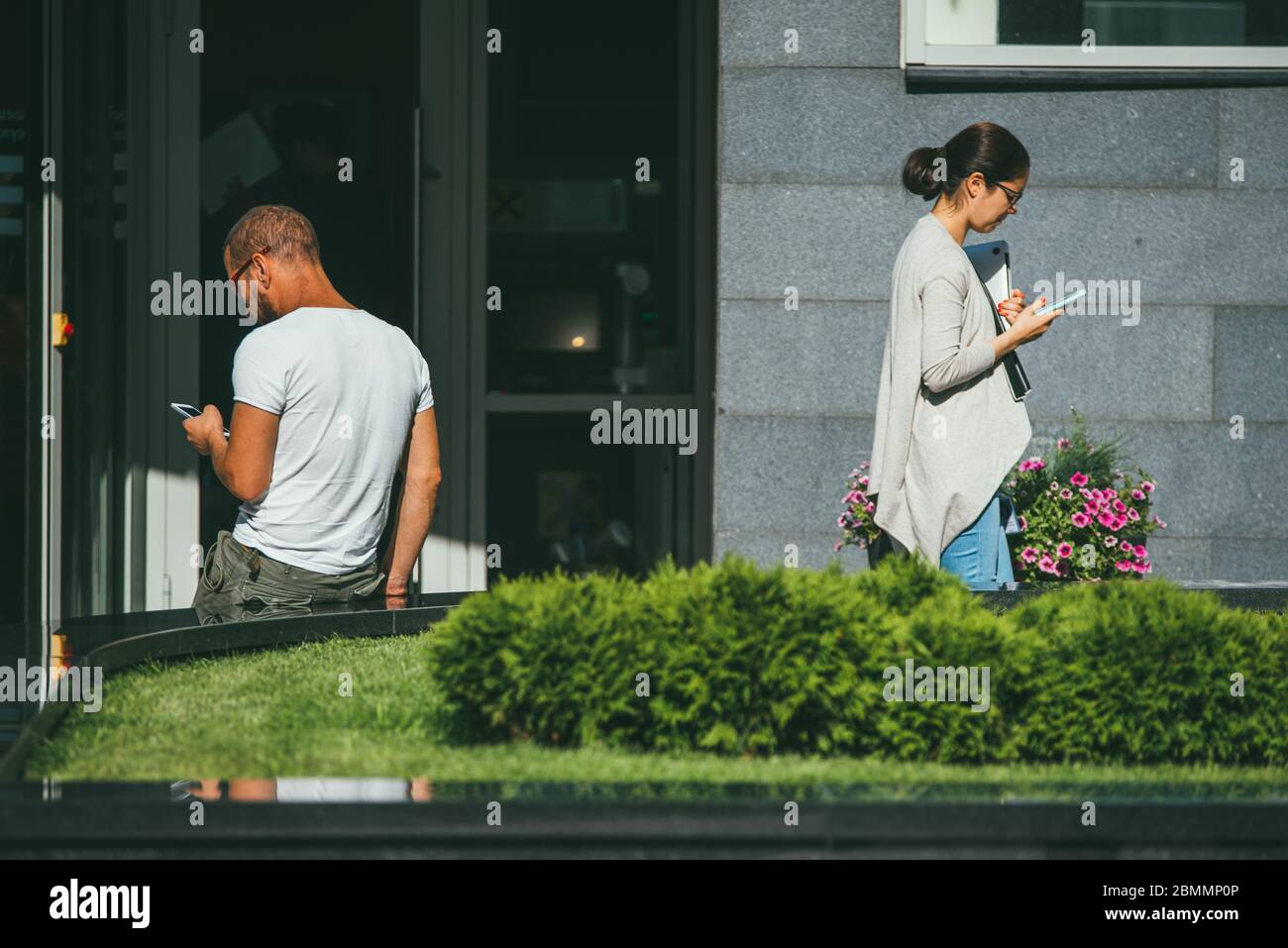 Moscow, Russia - AUGUST 31, 2017: A young man and woman stand and use their phones keeping a social distance from each other on the streets of a Stock Photo
