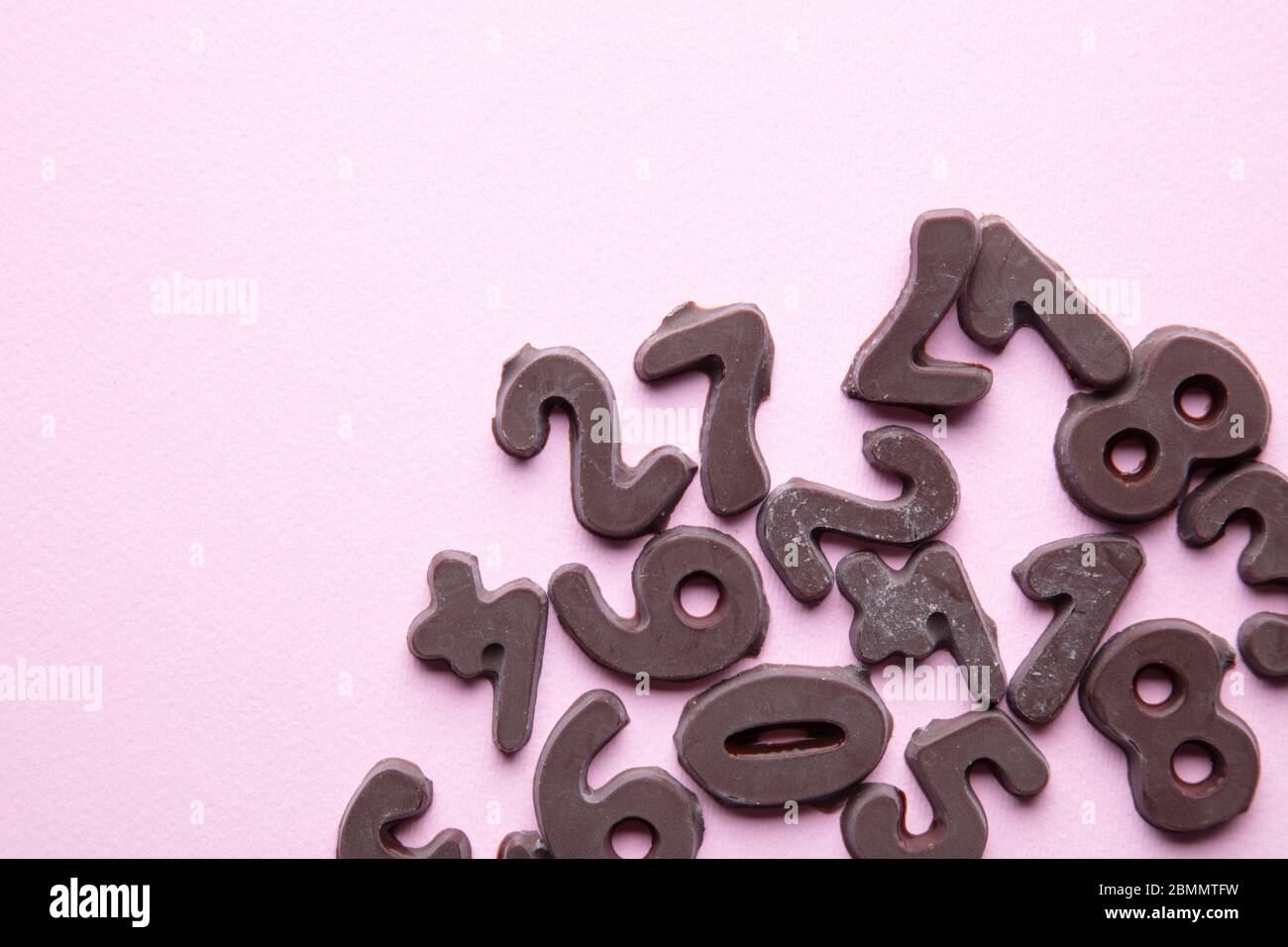 an artsy studio shot of chocolate numbers against a pastel pink  background Stock Photo