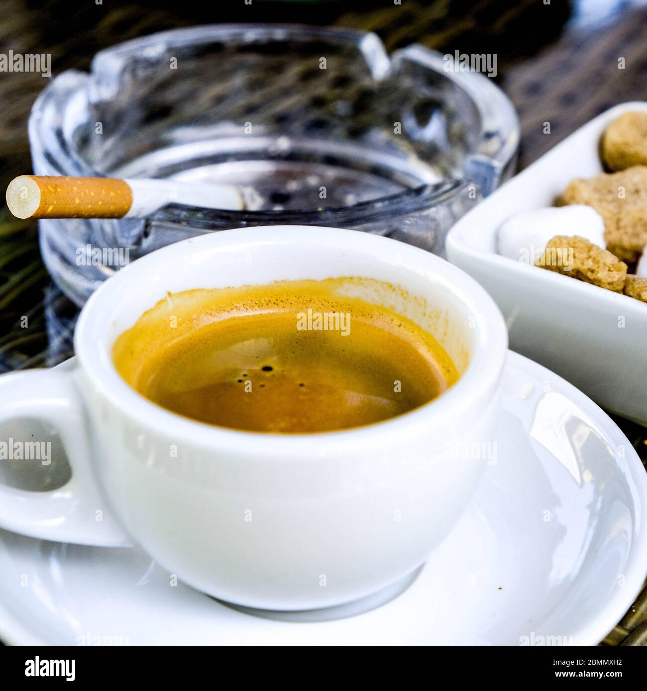 cigarette and espresso Cup Of Strong Espresso Coffee Wirth A Sugar Bowl And A Lit Cigarette In A  Glass Ashtray, With No People Stock Photo