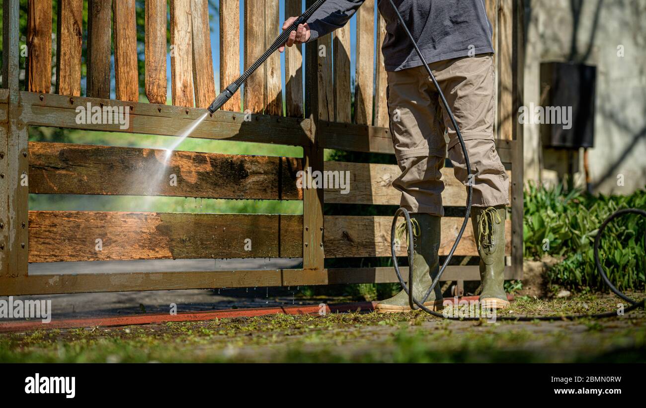 Unrecognizable man cleaning a wooden gate with a power washer. High ...