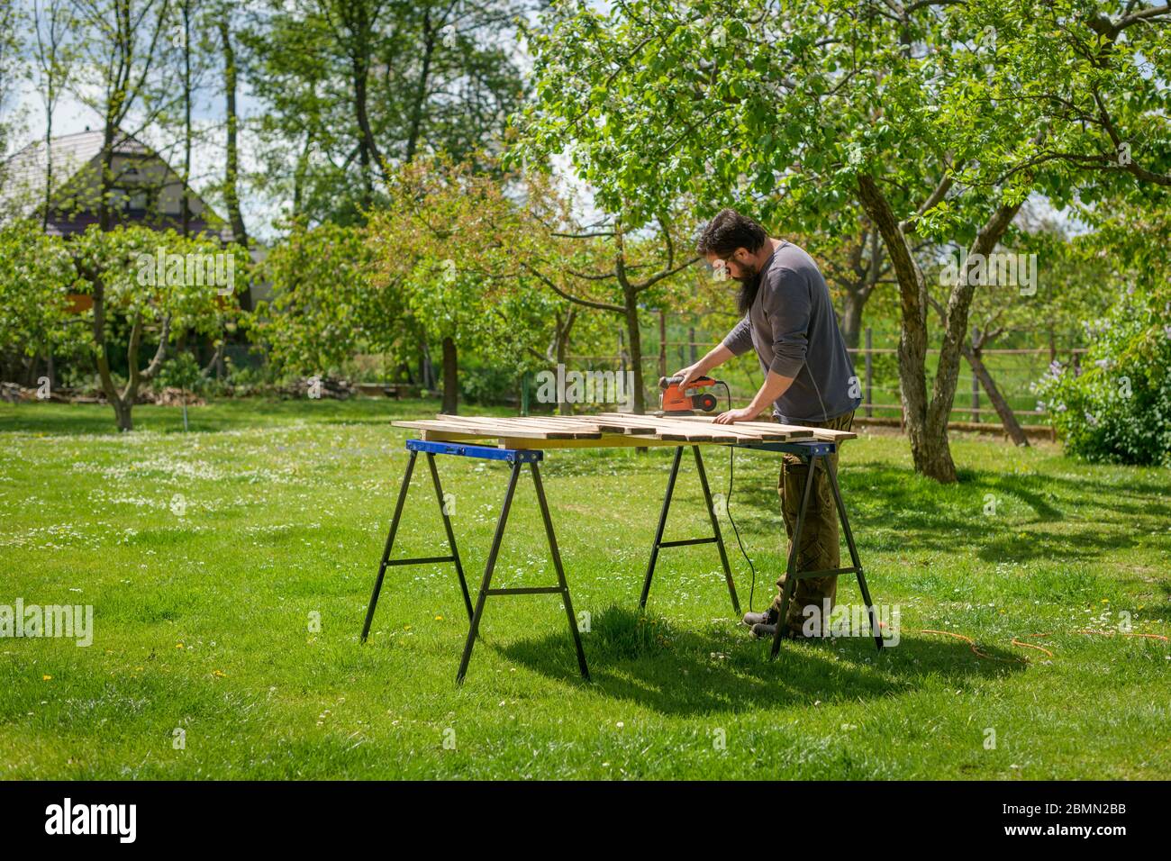 Mid adult caucasian man in the garden sanding wooden planks. DIY home improvement, restoration, carpentry concept. Stock Photo