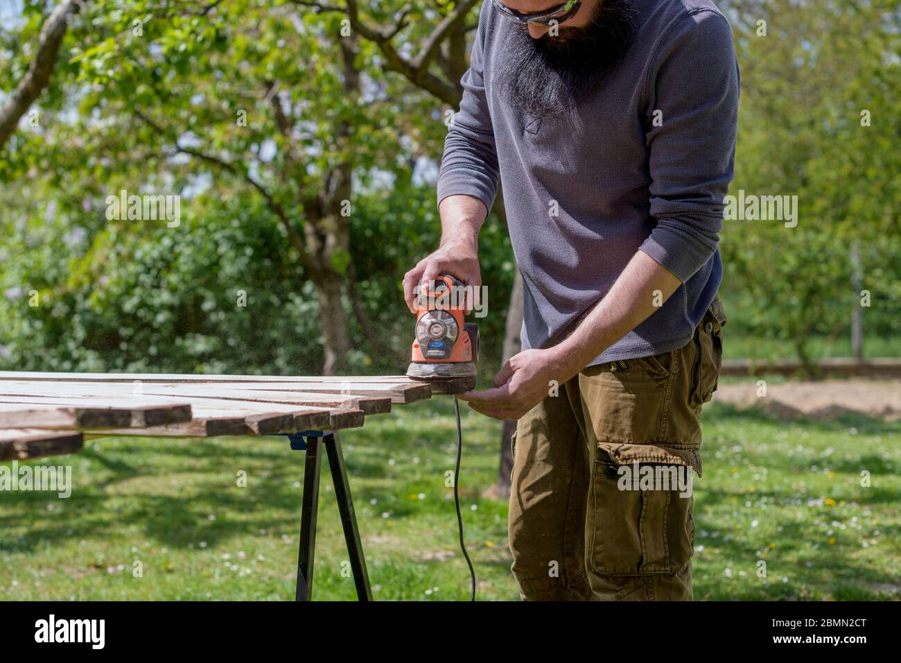 Mid adult caucasian man in the garden sanding wooden planks. DIY home improvement, restoration, carpentry concept. Stock Photo