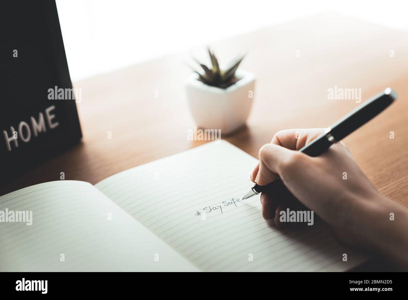Woman hand with pencil writing stay safe on notebook at home desk. Work from home and quarantine concept on epidemic outbreak. Stock Photo