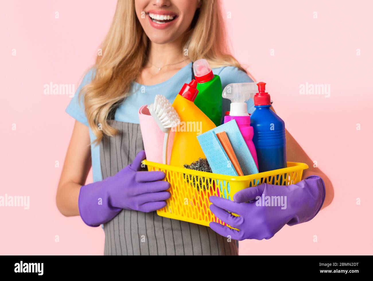 Focus on basket of cleaning supplies. Housewife in apron and purple rubber gloves Stock Photo