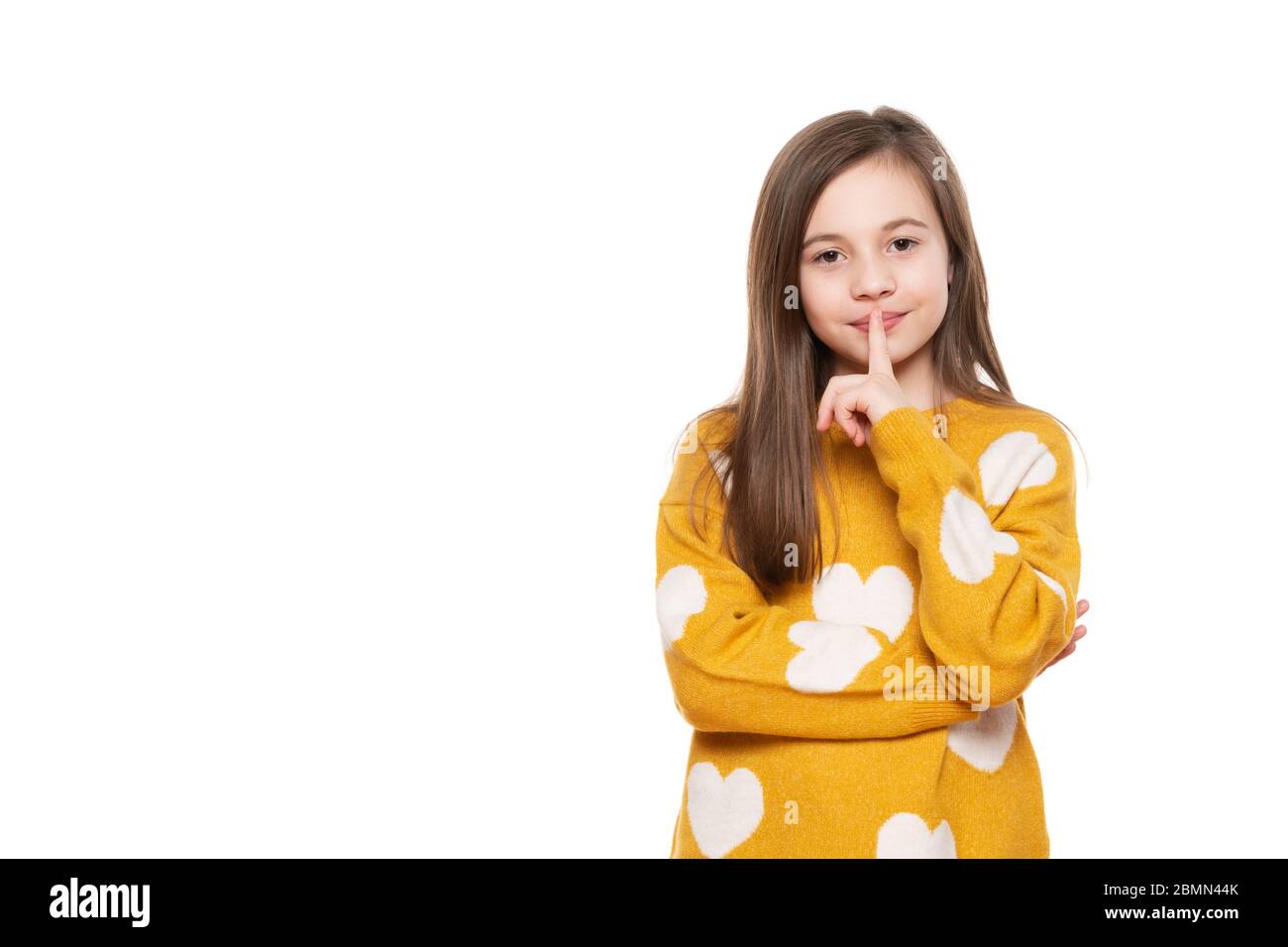 Finger on lips, silent gesture. Shhh! Waist up portrait of a charming young schoolgirl showing silence symbol, holding forefinger on lips, looking at Stock Photo